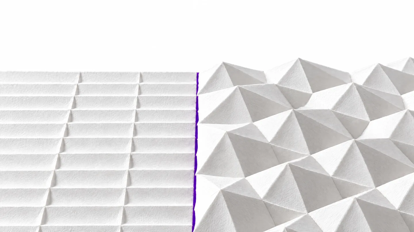 Eine Origami-Tessellation aus weißem Papier. Links liegen flache, geordnete Falten, rechts steigen dieselben Falten zu Facetten auf. Dazwischen verläuft eine violette Linie.